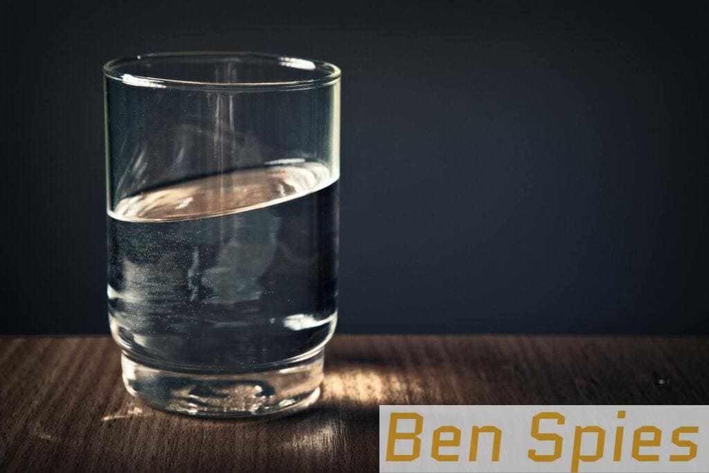 A clear glass of water sitting on a wooden table against a dark background.